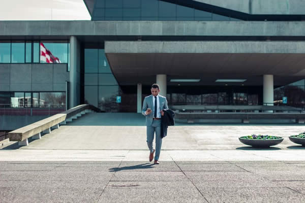 Businessman looking at phone walks outside a building.