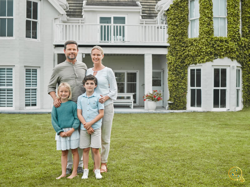 A family of a husband, wife, young son, and young daughter standing in front of their house posing for a photo