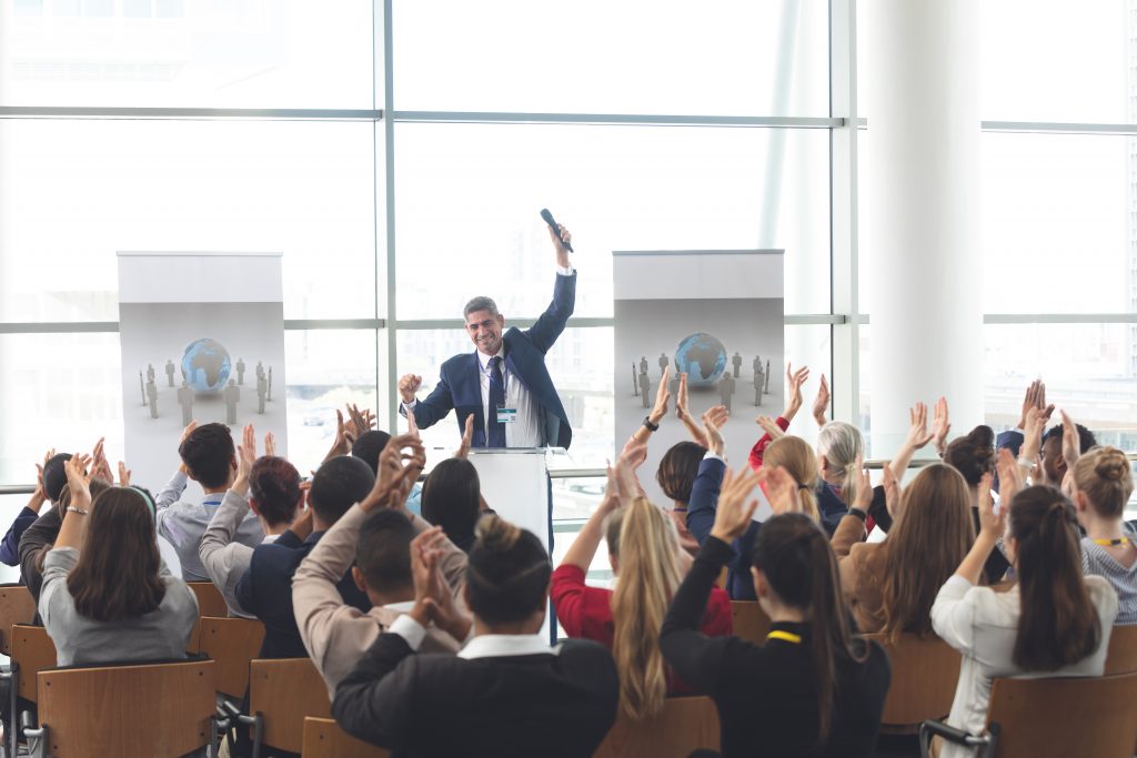 A professional speaker excitedly speaking in front of a group about the benefits of marketing for speakers Industries