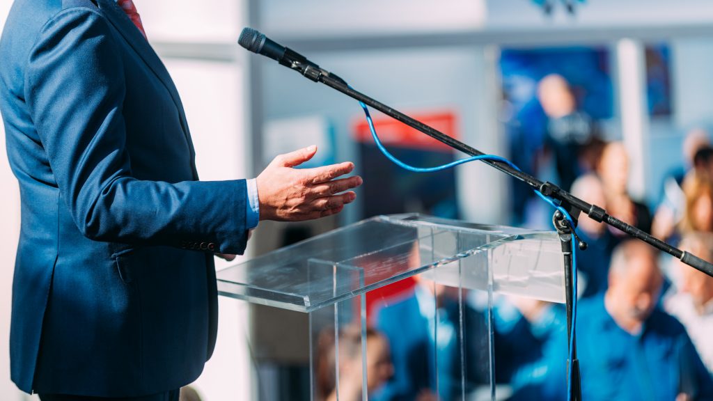 A businessman in front of an audience speaking about the unique benefits of COS Marketing Agency