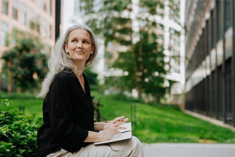 A woman with gray hair outside holding a laptop thinking about digital marketing for authors