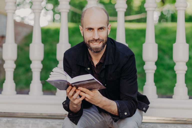 A young man holding a book thinking about digital marketing for authors